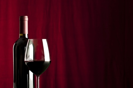 a glass of red wine and a bottle on red backgroundの写真素材
