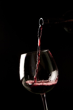 Red wine splash on a glass on black background.の写真素材