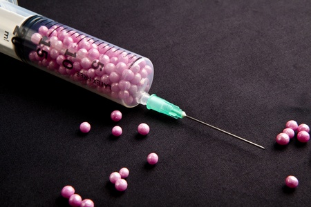 Syringe filled with pink candy on a black backgroundの写真素材