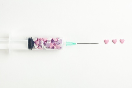 Syringe filled with heart shaped candy on a white backgroundの写真素材