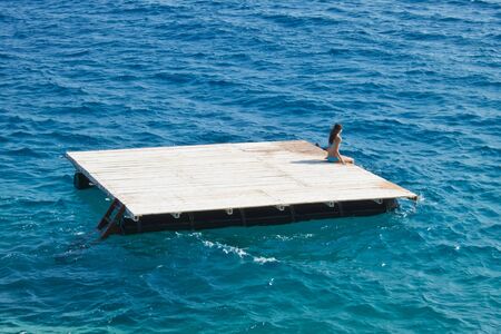 young woman relaxing  on a wooden raft in the seaの写真素材