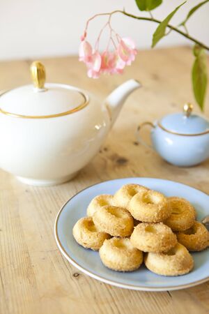 a plate of biscuits, a tea pot and a flower on wooden tableの写真素材