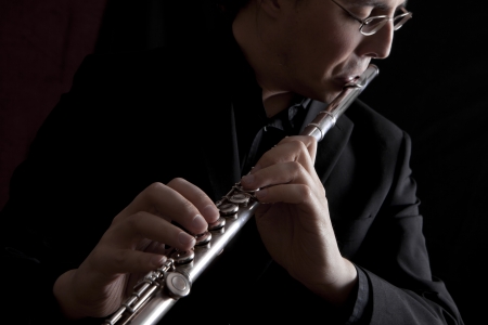 professional flutist musician playing flute on black backgroundの写真素材