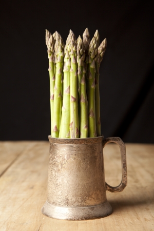 Bunch of fresh green asparagus in a mug on wooden tableの写真素材