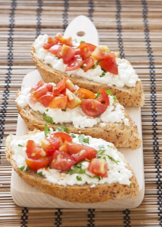 Crostini with cottage cheese, parsley and tomato on cutting boardの写真素材