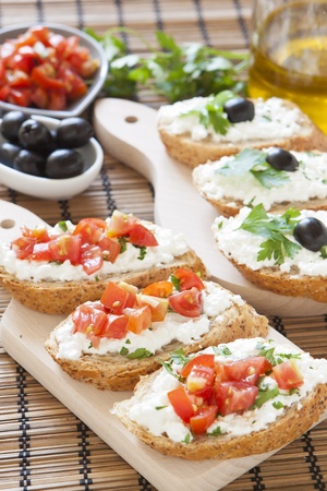 Crostini with cottage cheese, parsley, tomato and olives on cutting boardの写真素材