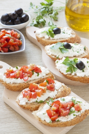 Crostini with cottage cheese, parsley, tomato and olives on cutting boardの写真素材