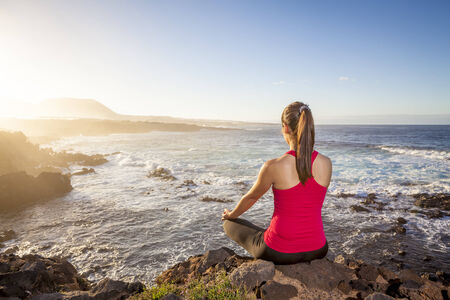 young woman practicing yoga meditation on the beach at sunsetの写真素材