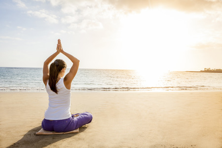 young woman practicing yoga meditation on the beach at sunsetの写真素材