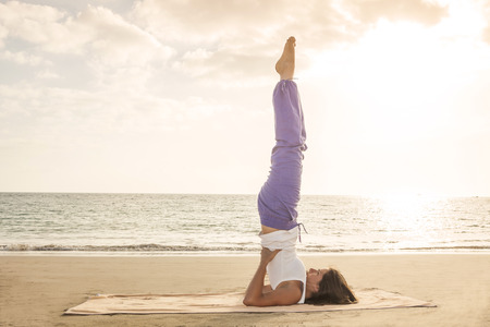 Young woman practicing yoga candle pose on the beach near the ocean at sunset