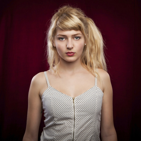 portrait of a young beautiful blonde woman on red velvet backgroundの写真素材