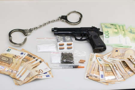 A shipment of drugs seized from dealers by the police, consisting of smuggled drugs in capsules, sachets of powdered cocaine and marijuana or ganja, and a pile of euro money from the saleの写真素材