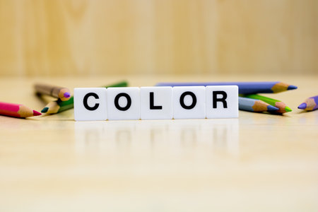 A row of small white plastic tiles, containing the letters forming the word color, placed on a table together with a colored pencils, to represents the concept of colors and design.の写真素材