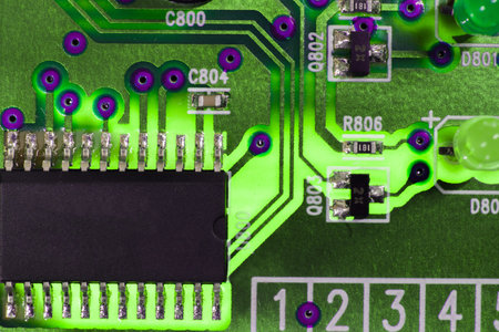 The close-up photo of a green electrical circuit, with the light passing through it thanks to the backlight, on the circuit is a small integrated circuit soldered to the board.の写真素材