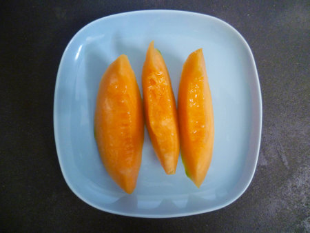 Three slices of melon on a blue ceramic plate from aboveの写真素材