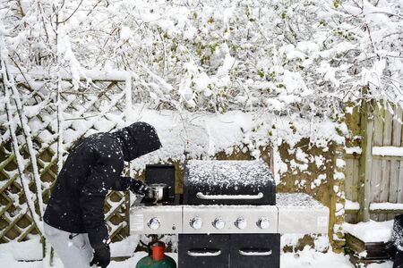 Portrait of a man cooking food on the barbecue on a snowy day due to a powercutの写真素材