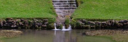 Panoramic photo of a waterfall flowing down stairs in an ornamental gardenの写真素材