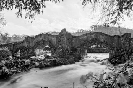 Long exposure of a waterfall flowing under a bridge on the river Avill in Dunster