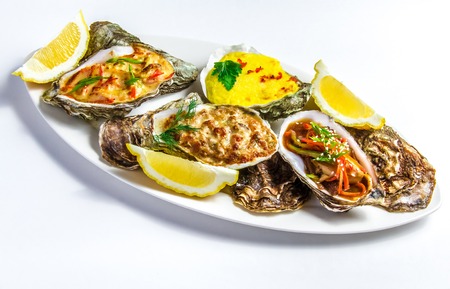 Dish with baked oyster shell with cheese, salad oysters, served greens and lemon on a White backgroundの写真素材