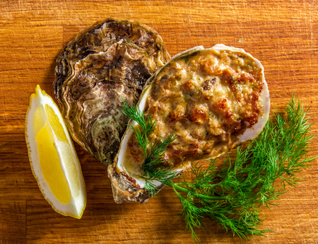 Baked oyster shell with cheese,  served with greens and lemon on a wooden background.