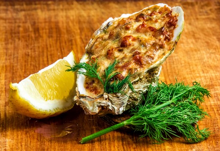 Baked oyster shell with cheese,  served with parsley and lemon on a wooden background.の写真素材