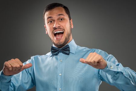 Closeup portrait of excited, energetic, happy, smiling man in blue shirt and butterfly tie is gesturing with his hand, pointing finger shows itself. Positive human emotion facial expressionの写真素材