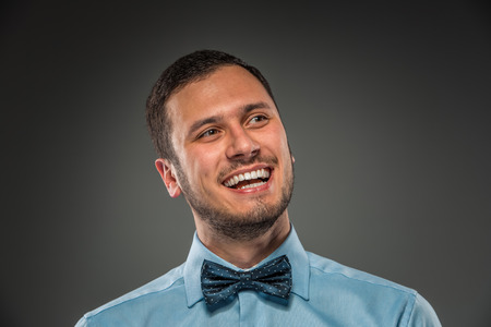 Portrait of happy smiling young man in blue shirt and butterfly tie  isolated over gray studio background. Closeupの写真素材