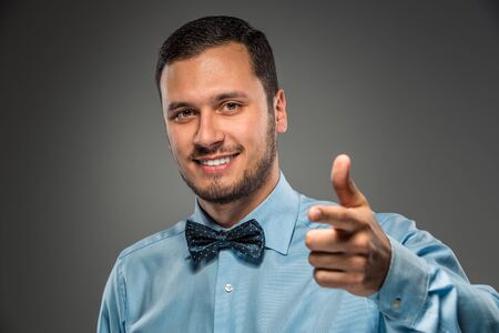 Closeup portrait of excited, energetic, happy, smiling man in blue shirt and butterfly tie  is gesturing with his hand, pointing finger at camera. Positive human emotion facial expressionの写真素材