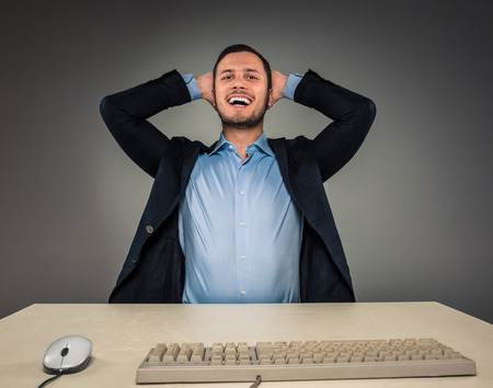 Closeup portrait of excited, energetic, happy, man in blue shirt and butterfly tie winning, his hands kept his head sitting at a desk near a computer. Positive human emotion facial expressionの写真素材
