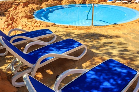 Closeup several of sun loungers by a beautiful swimming pool. Exotic vacation by the hotel pool in...
