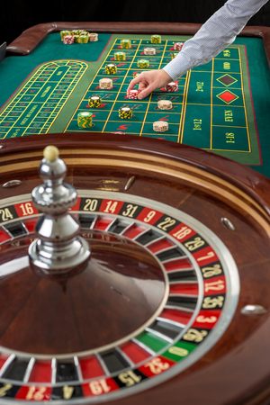 Close up view of Roulette and piles of gambling chips on a green table in casino. Man hand over casino chips on roulette tableの写真素材