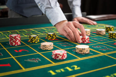 Picture of a green table and betting with chips. Man hand over casino chips on roulette table. Close upの写真素材