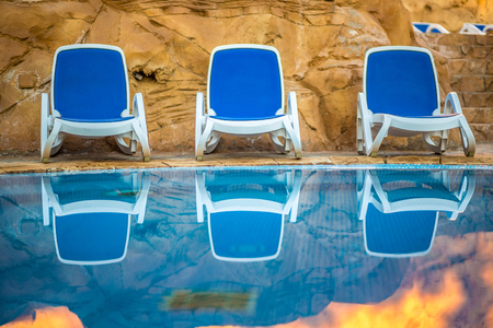 Three sunloungers near beautiful swimming pool and reflected their in a blue water of the pool. Exotic vacation in Egypt.の写真素材