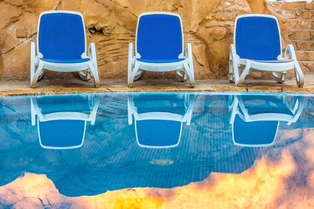 Three sunloungers near beautiful swimming pool and reflected their in a blue water of the pool. Exotic vacation in Egypt.の写真素材
