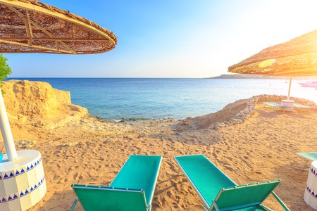 Sun umbrella and empty deckchairs on the shore sand beach with view on blue sea, Egypt.の写真素材
