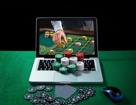 Green table with casino chips, cards on notebook, image of poker player on screen of laptop. Concept...