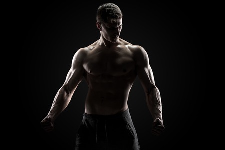 Sexy muscular man posing with naked torso in studio and looking behind on black backgroundの写真素材