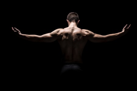 Rear view of healthy muscular young man with his arms stretched out on black backgroundの写真素材