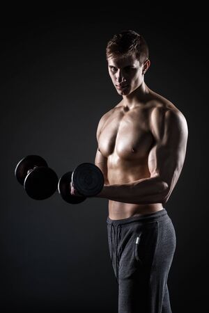Handsome muscular man showing perfect body with dumbbells and looking at the camera on black background.の写真素材