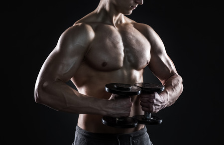 Mighty fitness man showing his gread body with dumbbells in hand on black background. Close-upの写真素材