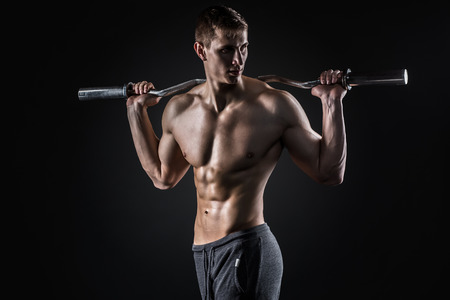 Strong man holding a barbell on his shoulders and looking to the side, on black backgroundの写真素材