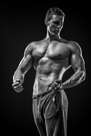 Image of very muscular man posing with naked torso in studio and looking behind on black background. Black and whiteの写真素材