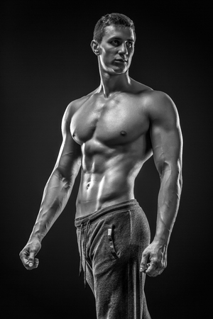 Image of very muscular man posing with naked torso in studio and looking behind on black background. Black and whiteの写真素材