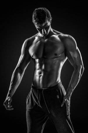 Sporty and healthy man posing and showing his perfect boddy on black background. Black and whiteの写真素材