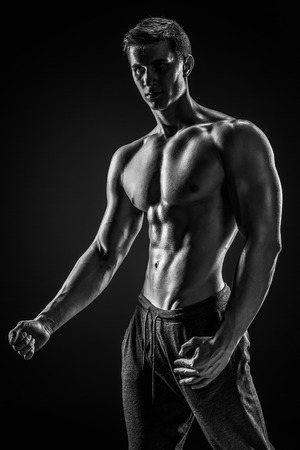Sexy shirtless bodybuilder posing and looking at camera on black background. Extreme strength, muscles and fitness.. Black and whiteの写真素材