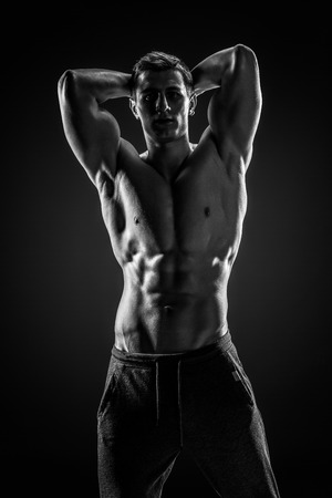 Sexy shirtless bodybuilder posing and looking at camera on black background. Extreme strength, muscles and fitness.. Black and whiteの写真素材