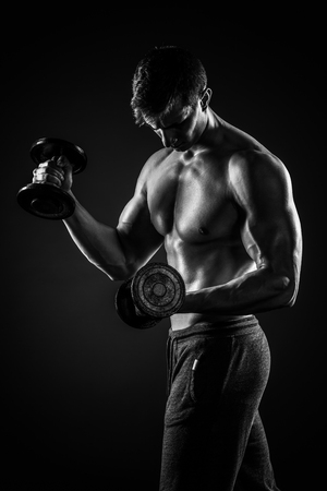 Athletic man showing muscular body and doing exercises with dumbbells on black background.. Black and whiteの写真素材