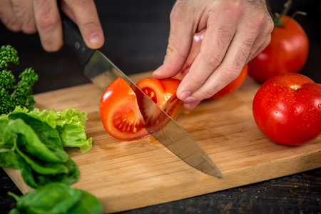 Close up on male hands cutting tomato, making salad. Chief cutting vegetables. Healthy lifestyle, diet foodの写真素材