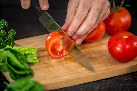 Close up on male hands cutting tomato, making salad. Chef cutting vegetables. Healthy lifestyle, diet foodの写真素材