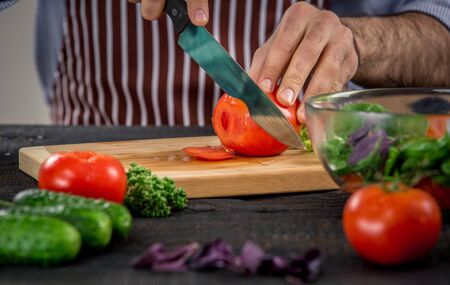 Close up on male hands cutting tomato, making salad. Chief cutting vegetables. Healthy lifestyle, diet foodの写真素材